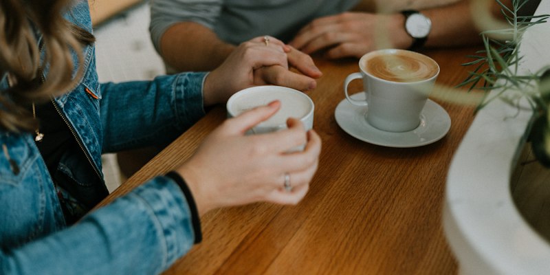 Two people holding hands over coffee at a café table